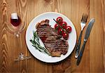 Sirloin steak with rosemary and cherry tomatoes on a plate with wine. View from above