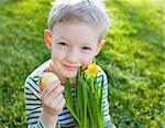 cute smiling little boy holding yellow bright easter egg and daffodils at spring time