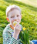 cute positive little boy holding colorful egg and pot with blooming daffodils at easter time