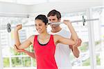 Male trainer helping happy young fit woman to lift the barbell in the gym