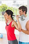 Male trainer helping young fit woman to lift the barbell in the gym