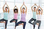 Portrait of a fit class standing in tree pose at a bright fitness studio