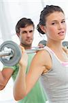 Fit young man and woman lifting barbells in the gym