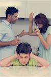 Sad young boy covering ears while parents quarreling in the kitchen at home