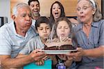 Extended family blowing candles on cake in the living room at home