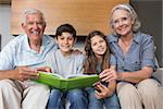 Portrait of happy grandparents and grandkids looking at album photo in the living room