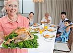 Portrait of a grandmother holding chicken roast with family at dining table in the house