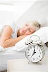 Blurred mature woman sleeping in bed with alarm clock in foreground at bedroom