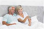 Happy mature couple watching tv in bed at home