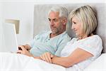 Concentrated mature couple using digital tablet in bed at home