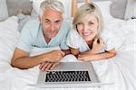 Portrait of a relaxed mature couple using laptop in bed at home