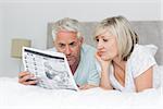 Relaxed mature couple reading newspaper in bed at home