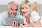 Smiling mature couple using digital tablet in bed at home