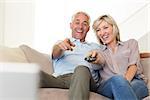 Cheerful mature couple watching tv on sofa at home