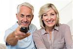 Portrait of happy mature couple watching tv on sofa at home