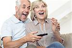 Cheerful mature couple watching tv on sofa at home
