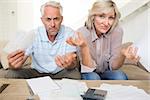 Tensed mature man and woman with bills and calculator sitting on sofa at home