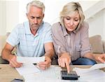 Concentrated mature man and woman with bills and calculator sitting on sofa at home