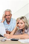 Tensed mature man and woman with bills sitting on sofa at home