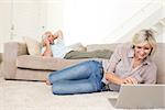 Mature woman using laptop while man on call in the living room at home
