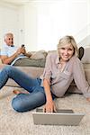 Mature woman using laptop while man text messaging in the living room at home