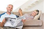 Mature man reading newspaper while woman text messaging in the living room at home