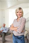 Portrait of a smiling woman with man reading newspaper in background at home