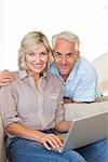 Portrait of a happy mature couple using laptop on sofa at home