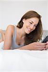 Pretty relaxed young woman text messaging in bed at home