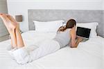Rear view of a relaxed young woman using laptop in bed at home