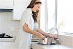 Side view of a young woman with vessel at the washbasin in the kitchen at home