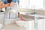 Closeup mid section of a woman pouring milk into dough at the kitchen