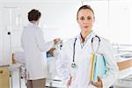 Portrait of confident doctor with colleague checking patient in background at hospital