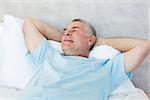 Senior man with hands behind head day dreaming in bed