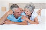 Happy senior couple smiling together while lying on bed at home