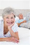 Portrait of smiling senior woman with man in background on bed at home