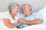 Romantic senior couple holding hands in bed at home