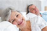 Portrait of happy senior woman lying on bed with man at home
