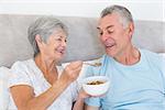 Happy senior woman feeding cereals to husband at home