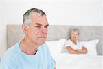 Sad senior man looking away with woman in background at home