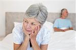 Sad senior woman looking away with man in background on bed at home