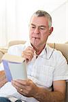 Concentrated man reading book while sitting on sofa at home