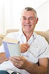 Portrait of smiling senior man holding book and glasses at home