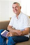 Portrait of senior man with book siting on sofa at home