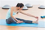 Full length of a sporty young woman stretching hand to leg in fitness studio