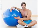 Full length portrait of a shirtless man with fitness ball sitting in the gym