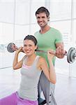 Male instructor helping fit woman to lift barbell in the gym