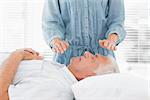 Female therapist performing Reiki over senior man at health spa