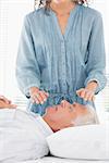Female therapist performing Reiki over face of senior man at health spa