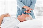 Massage therapist performing Reiki over forehead of senior man at health spa